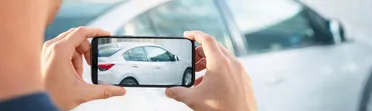 Hands holding a smartphone to photograph a car for an AutoScout24 listing